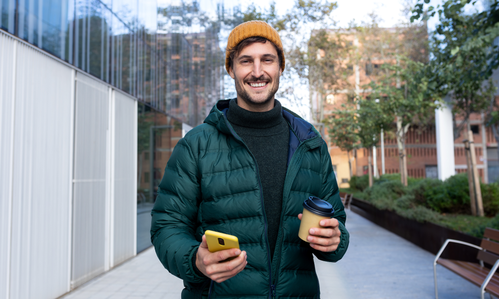 man green coat yellow hat phone coffee