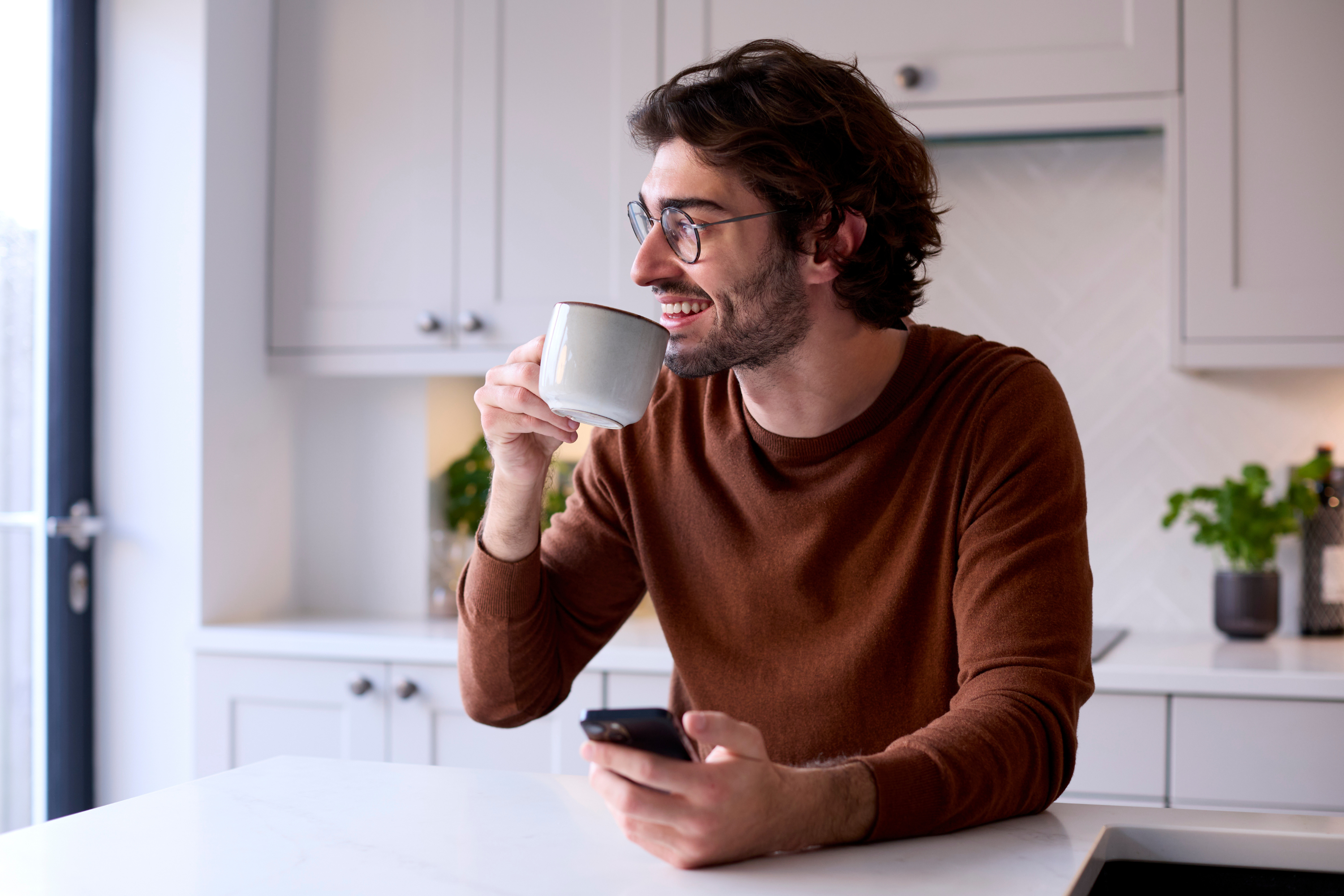 man relaxing kitchen holding coffee mobile phone