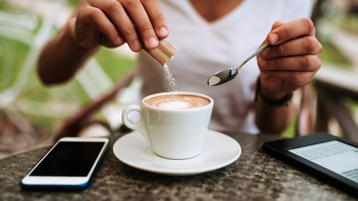 person putting sugar in coffee