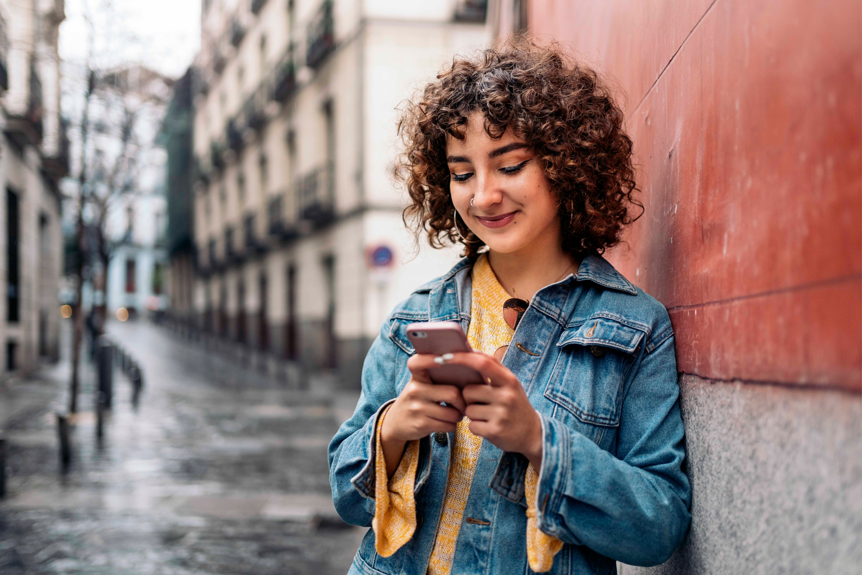 woman curly hair denim jacket mobile phone