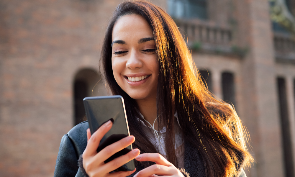 woman long hair smiles mobile phone street