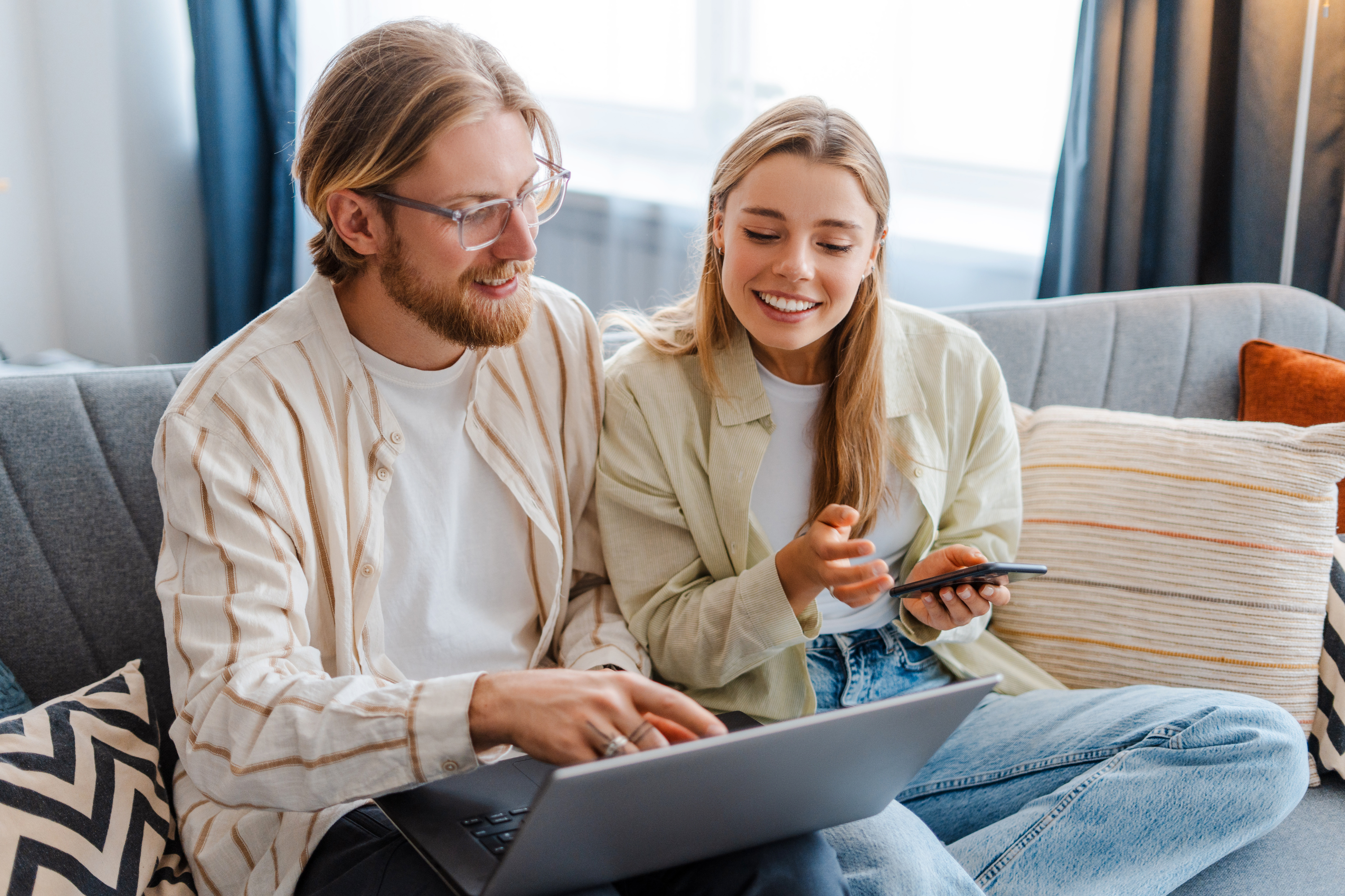 couple smiling browsing laptop mobile phone home