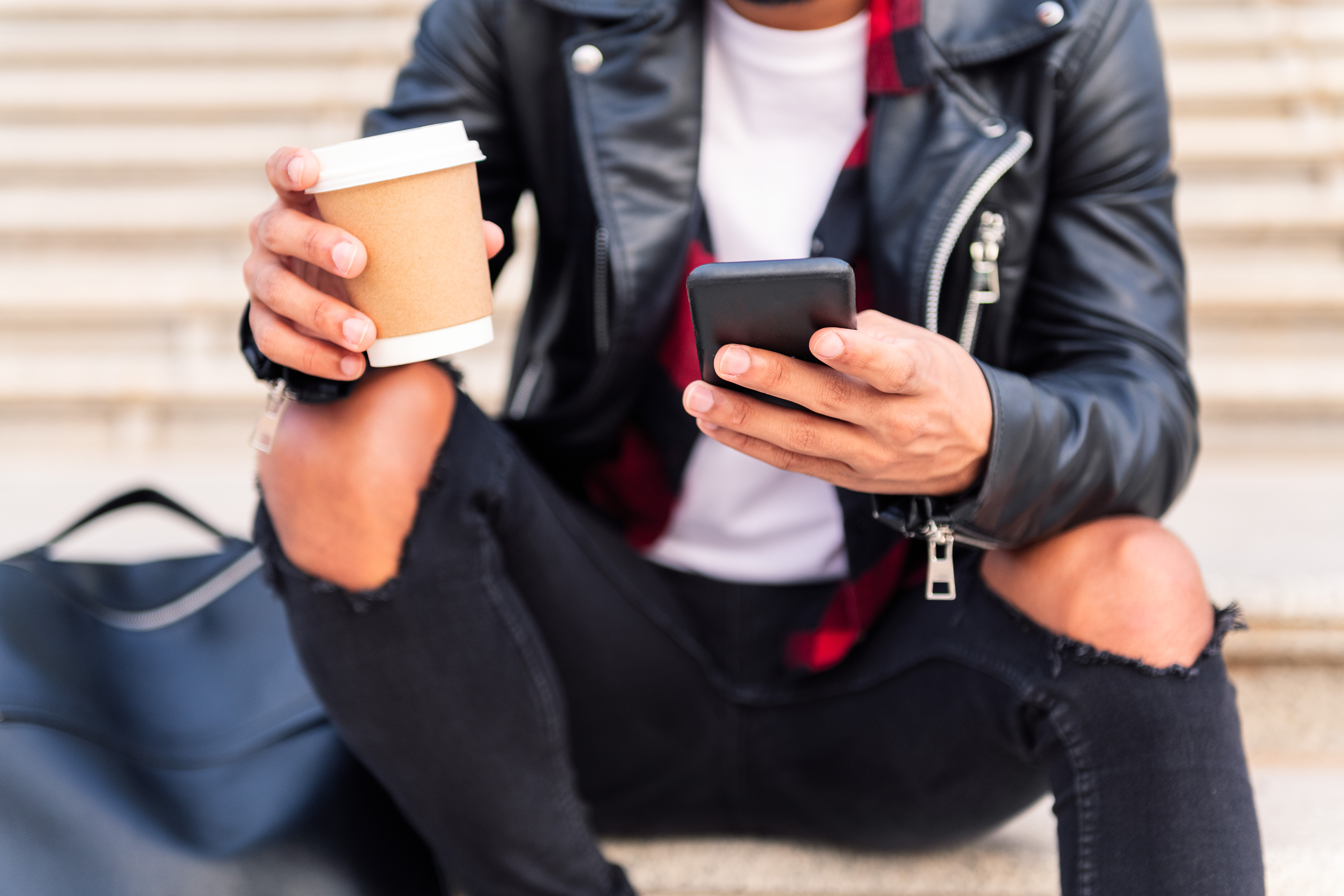 man leather jacket ripped jeans coffee phone