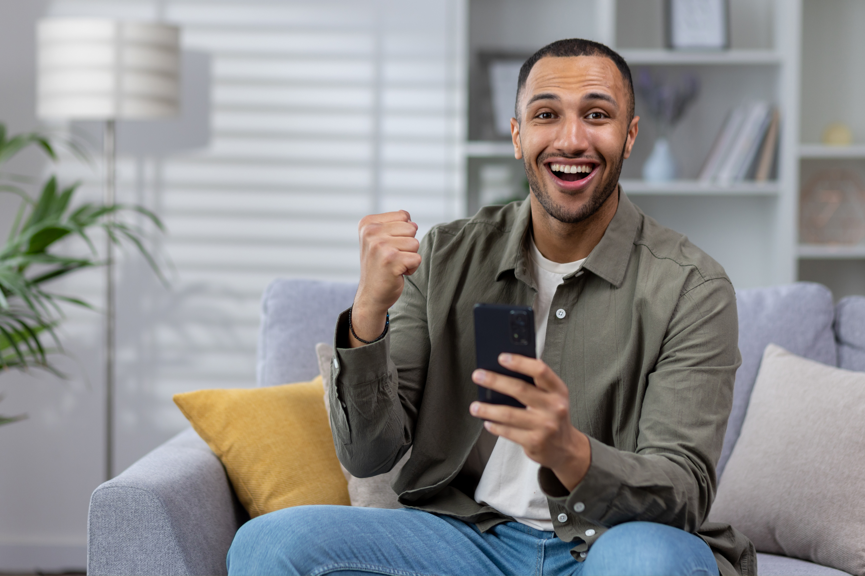 man smiling celebrating home couch mobile phone