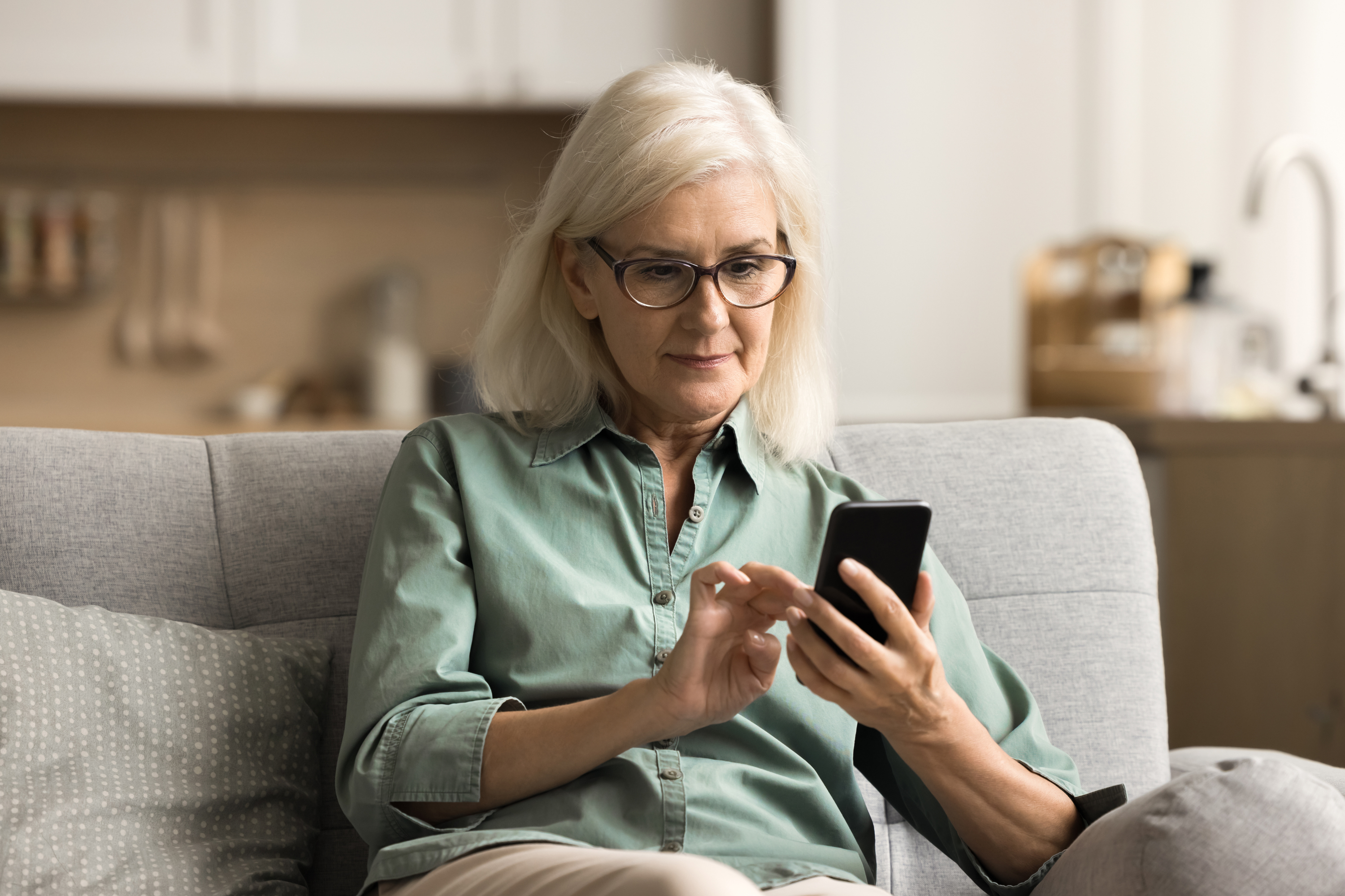 older woman sits couch mobile phone home