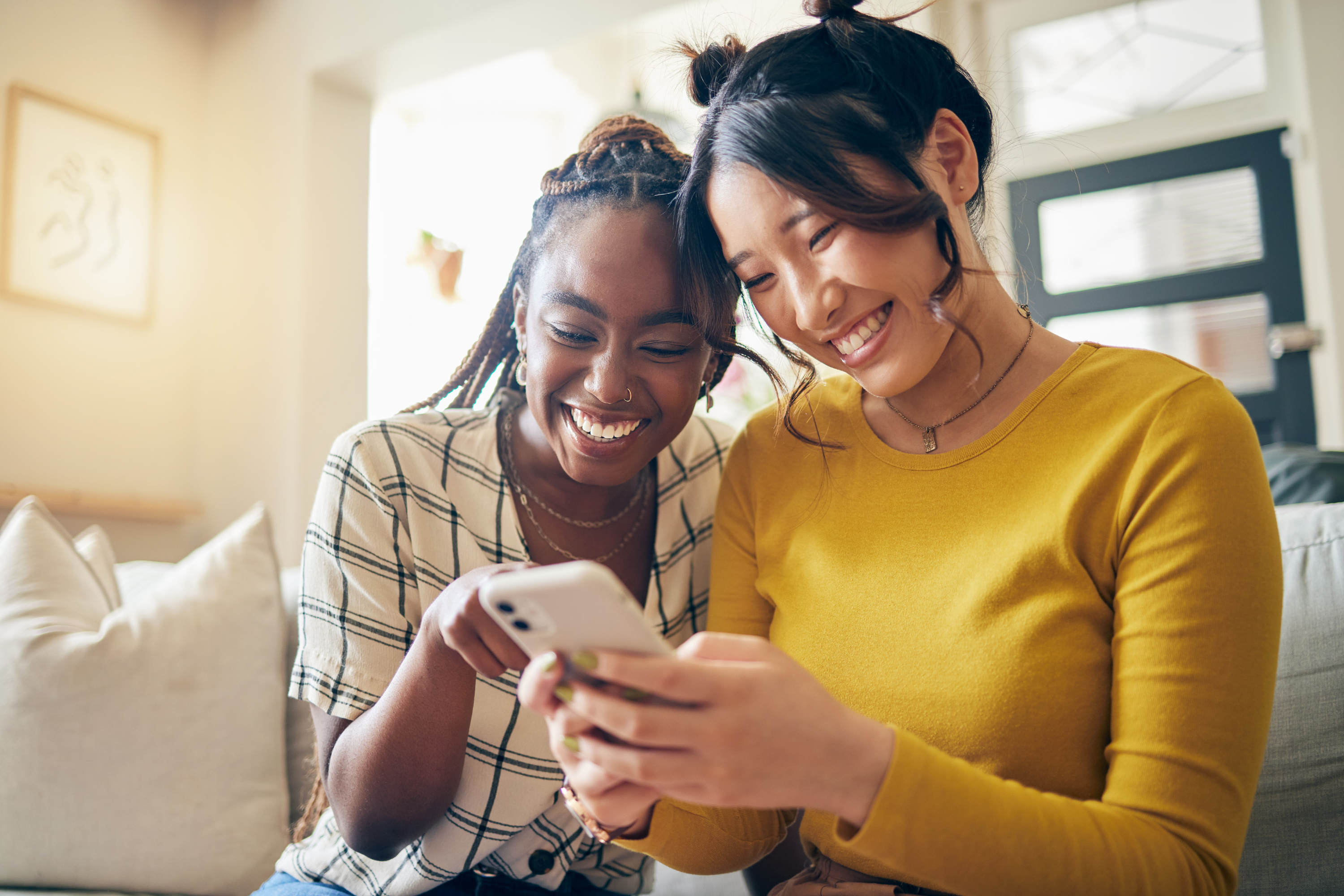 women friends smile cell phone sofa home