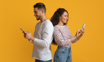 young couple back back yellow background mobile phones