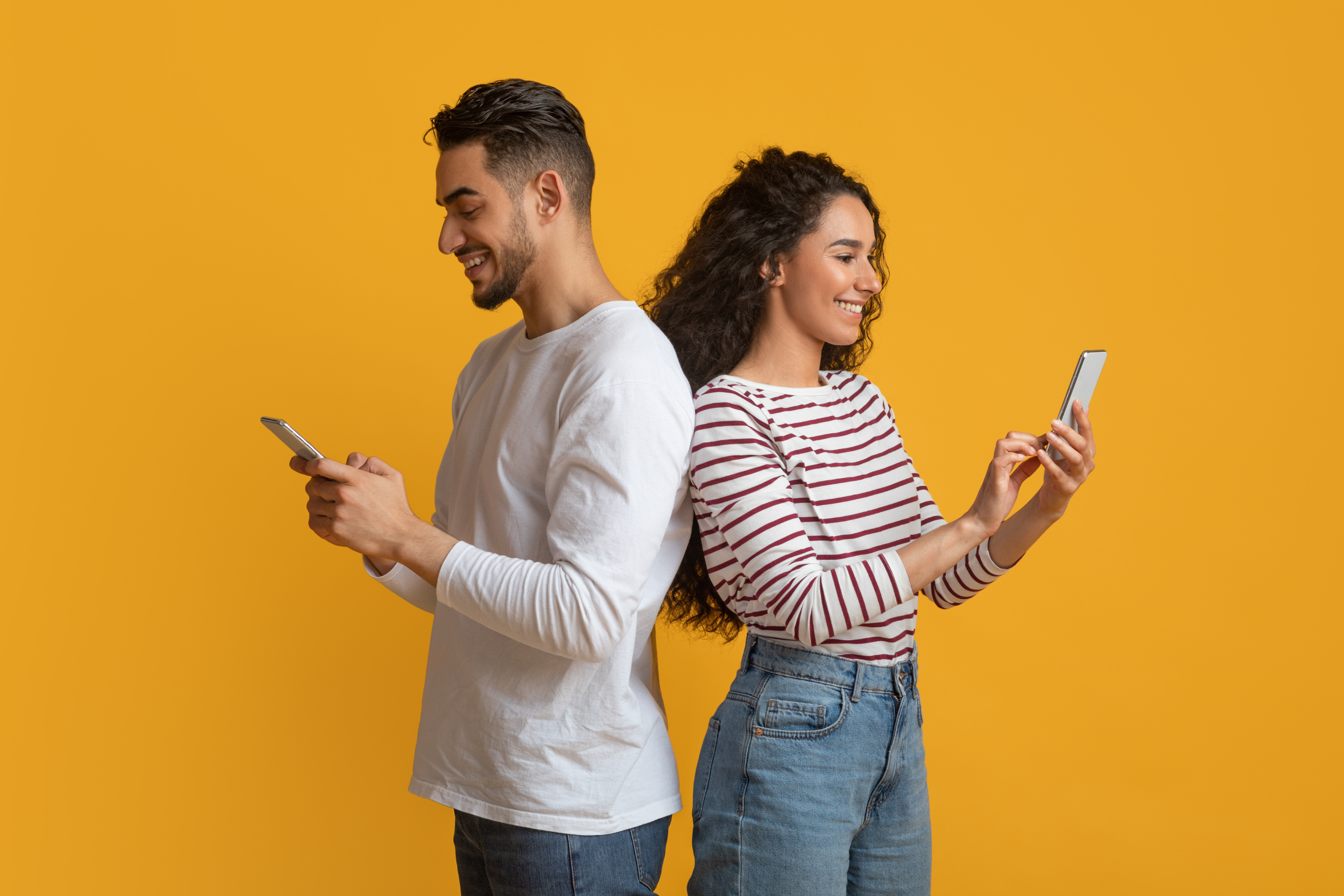 young couple back back yellow background mobile phones